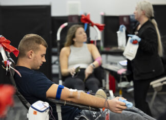 Greek Life partners with nonprofit on blood drives Undergraduate Eli Nelson reads his phone as he donates blood along with undergraduate Bridget White as she talks with team lead and phlebotomist Brittany Mark.