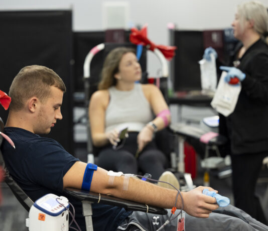 Undergraduate Eli Nelson reads his phone as he donates blood along with undergraduate Bridget White as she talks with team lead and phlebotomist Brittany Mark.