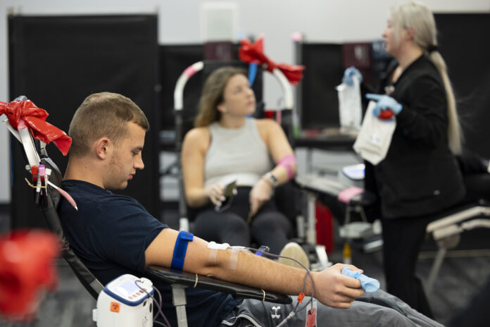 Undergraduate Eli Nelson reads his phone as he donates blood along with undergraduate Bridget White as she talks with team lead and phlebotomist Brittany Mark.