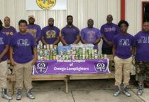 Members of the Omega Lamplighters, front row, and Omega Psi Phi Fraternity Inc., back row, stack food they collected during a food drive for Feed by Faith. Glenda Sanders / The Meridian Star