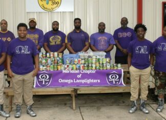 Members of the Omega Lamplighters, front row, and Omega Psi Phi Fraternity Inc., back row, stack food they collected during a food drive for Feed by Faith. Glenda Sanders / The Meridian Star