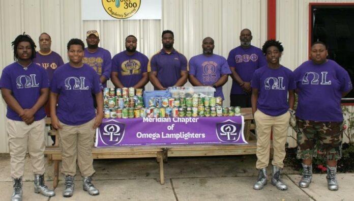 Members of the Omega Lamplighters, front row, and Omega Psi Phi Fraternity Inc., back row, stack food they collected during a food drive for Feed by Faith. Glenda Sanders / The Meridian Star
